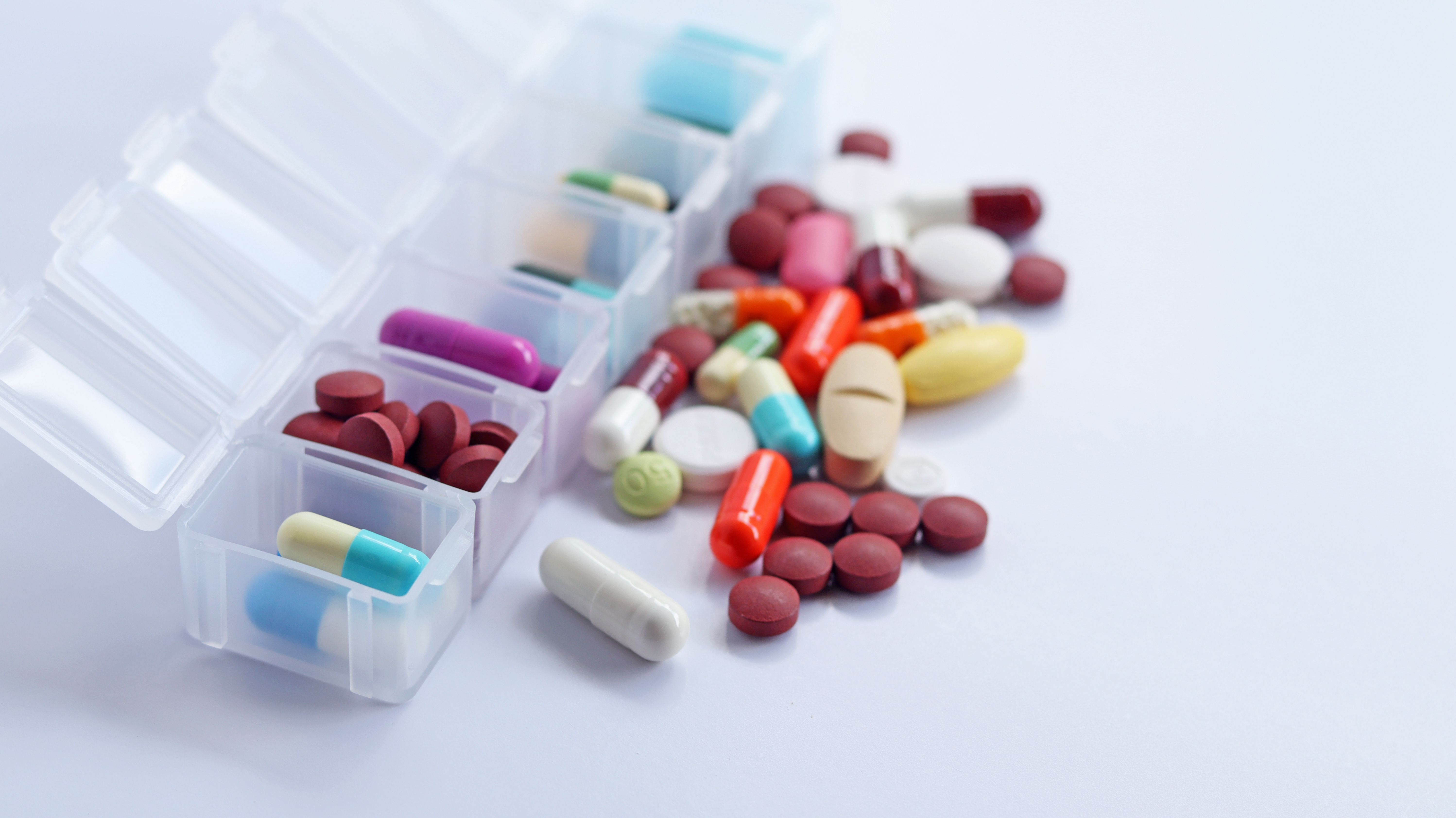 Pill box with colorful of pills, tablets, and capsules inside and outside of a pill box.