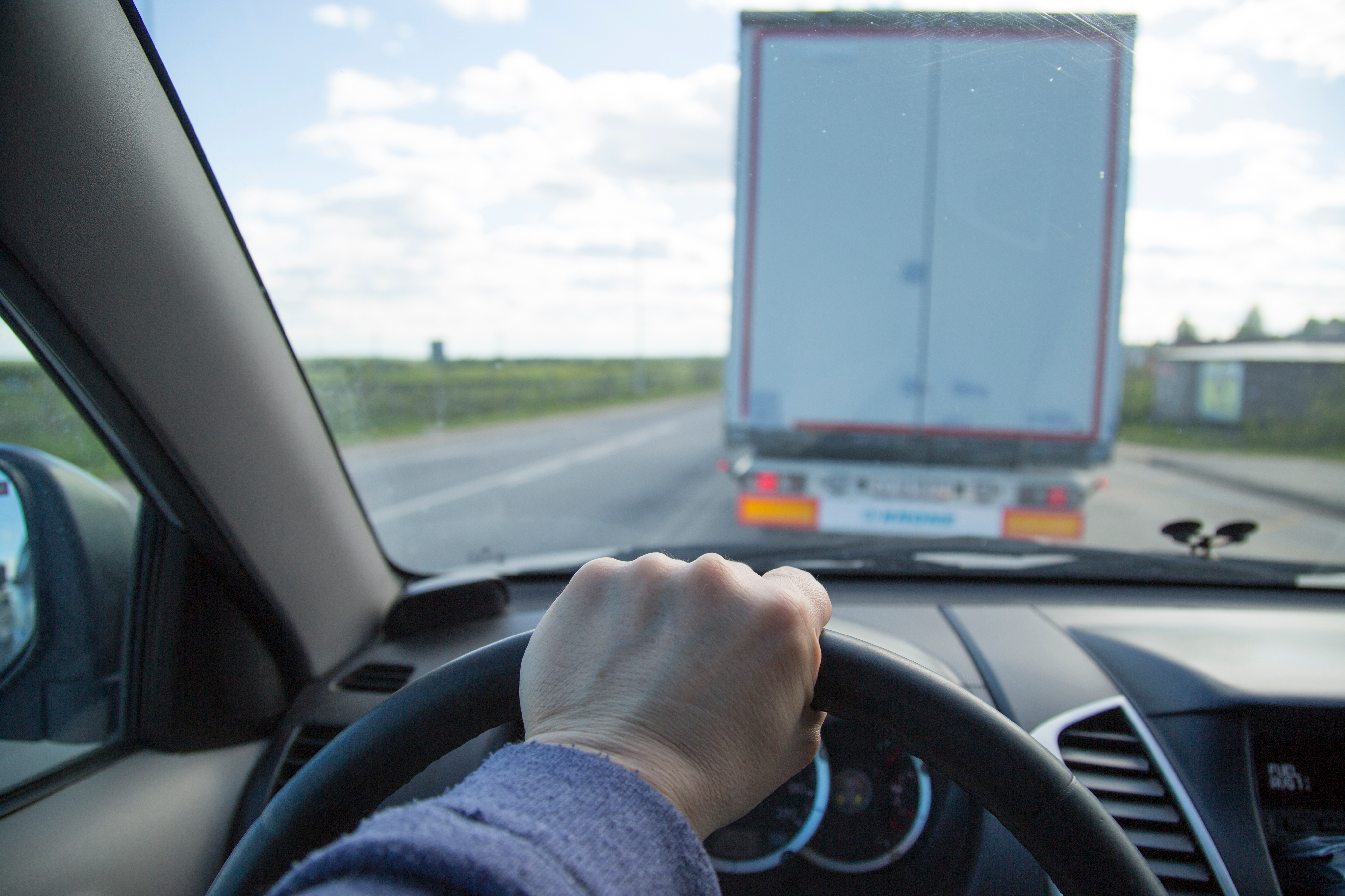 Driver behind the wheel of a passenger vehicle following a semi-truck on the highway.